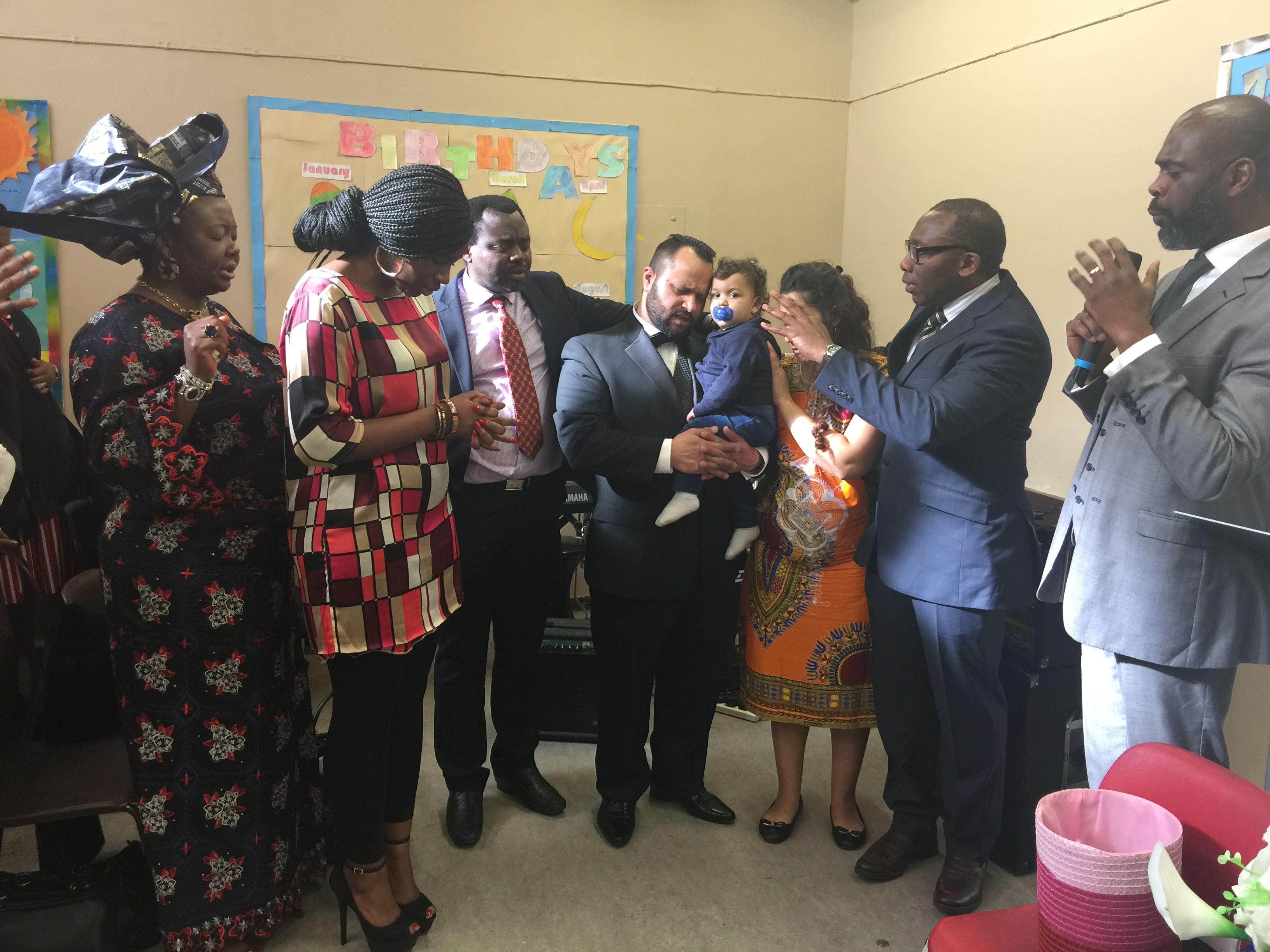 Church leaders and family praying during a baby dedication service